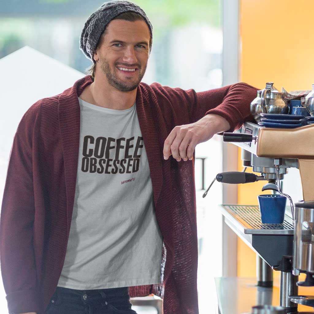 man leaning on coffee maker wearing a caffeiniac t-shirt with the COFFEE OBSESSED design