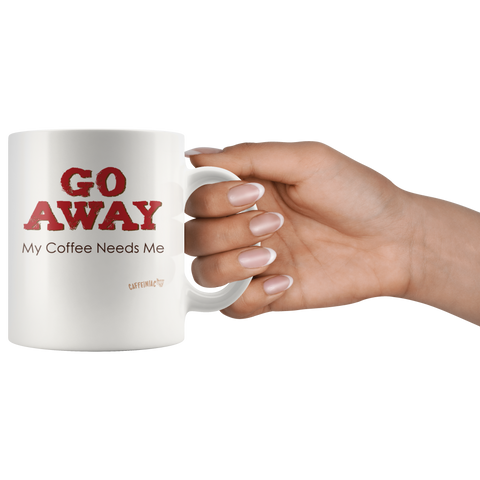 Image of a womans hand holding the handle of a white ceramic coffee mug with the Caffeiniac design GO AWAY My Coffee Needs Me on both sides