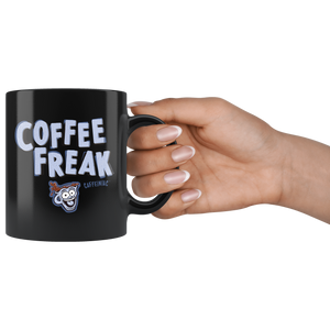 a woman's hand holding the handle of a black ceramic coffee mug with the Caffeiniac design COFFEE FREAK in light blue letters
