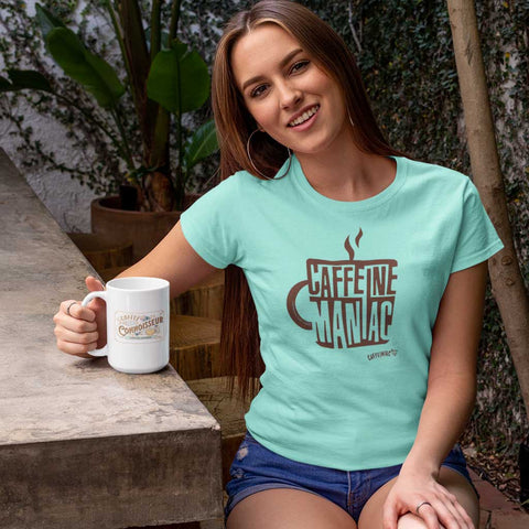 Image of smiling woman enjoying her coffee in teal tshirt by Caffeiniac with the design CAFFEINE MANIAC on the front