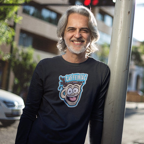 Image of smiling man leaning against a pole wearing a Next Level Mens Long Sleeve T-Shirt featuring the original Caffeiniac Dude cup design on the front