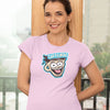 Woman standing against wall wearing a pink short sleeve shirt featuring the original Caffeiniac dude cup design on the front