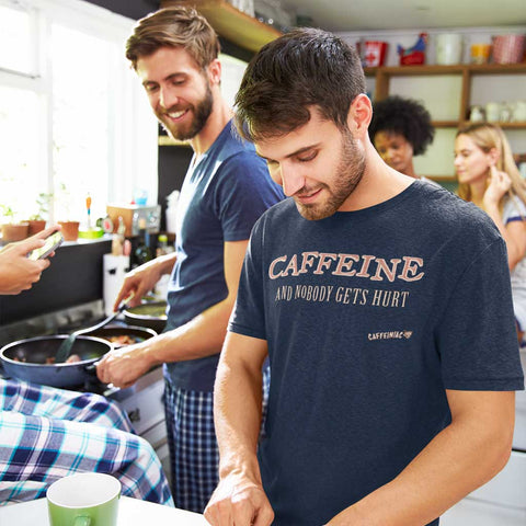Image of man cooking breakfast with friends and wearing a navy blue Caffeiniac t-shirt with the design CAFFEINE and nobody gets hurt on the front