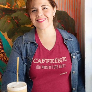 Smiling woman having an ice coffee wearing a jacket and red V-neck Caffeiniac shirt with the design CAFFEINE and nobody gets hurt