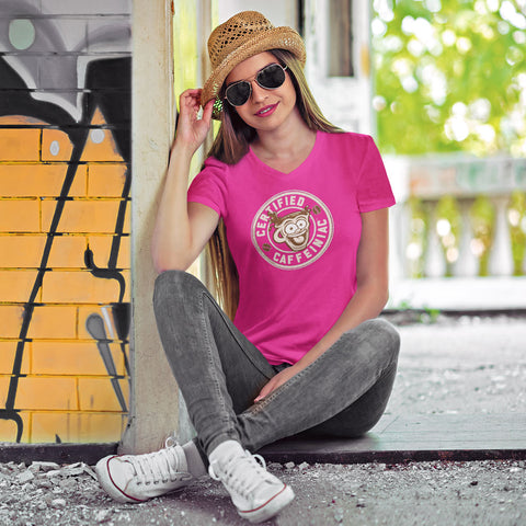 Image of Woman sitting wearing a hat and sunglasses in a pink v-neck shirt featuring the Certified Caffeiniac design on the front