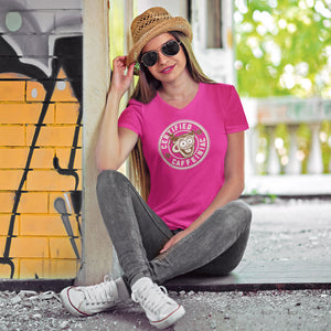 Woman sitting wearing a hat and sunglasses in a pink v-neck shirt featuring the Certified Caffeiniac design on the front