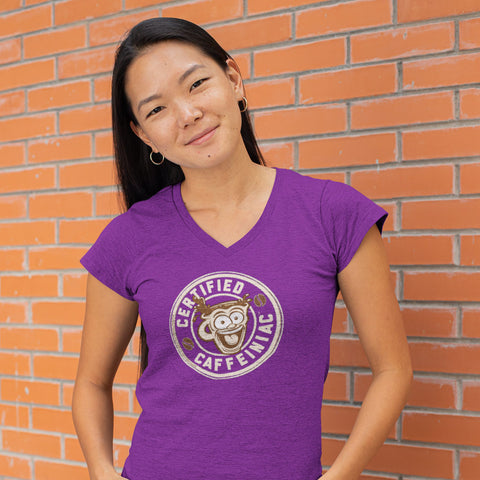 Image of smiling woman standing against a brick wall wearing a purple v-neck shirt featuring the Certified Caffeiniac design on the front