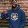 Man standing outdoors wearing a navy blue unisex hoodie with the Certified Caffeiniac design on front in tan ink