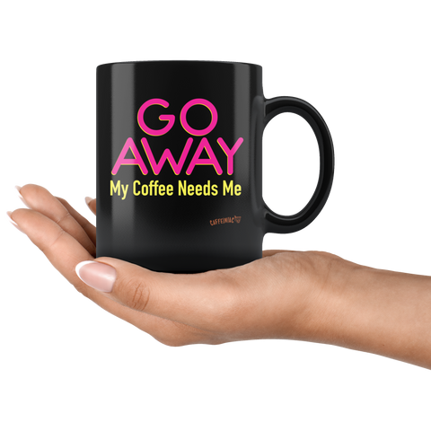 Image of a black coffee mug featuring the Caffeiniac design "GO AWAY My Coffee Needs Me" in vibrant color on front and back in the palm of a woman's hand