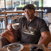 a man in a coffee shop drinking coffee wearing a coffee connoisseur t-shirt by caffeiniac