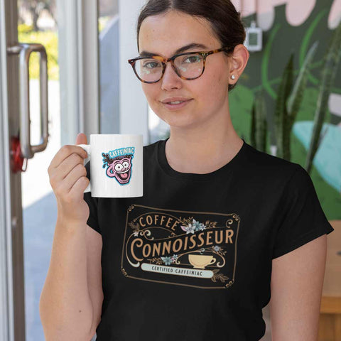 Image of woman in glasses drinking a cup of coffee wearing a black t-shirt with the coffee connoisseur design by caffeiniac