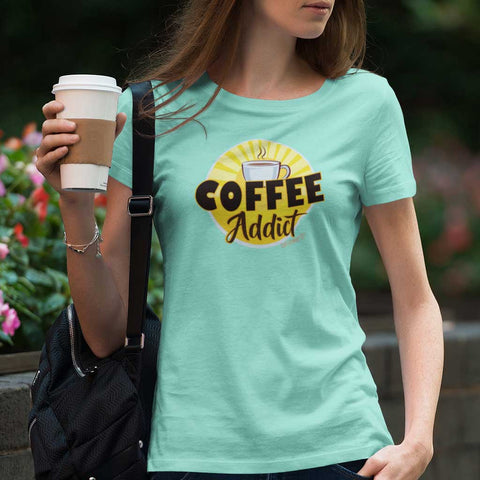 Image of woman holding a cup of coffee wearing a teal Caffeiniac shirt with the Coffee Addict design