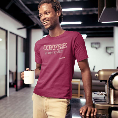 Image of a man in an office holding a cup of coffee wearing a dark red t-shirt featuring the Caffeiniac design Coffee and nobody gets hurt on the front in tan letters