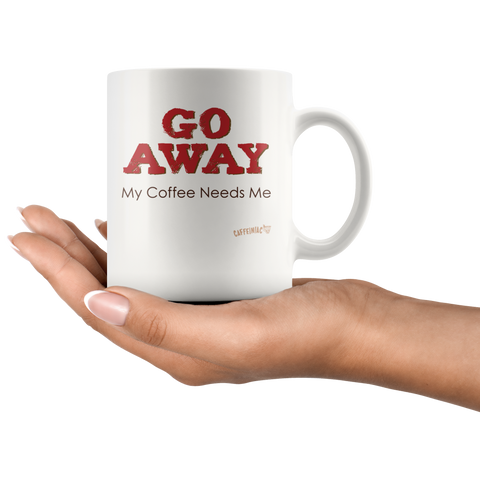 Image of a womans hand holding a white ceramic coffee mug with the Caffeiniac design GO AWAY My Coffee Needs Me on both sides