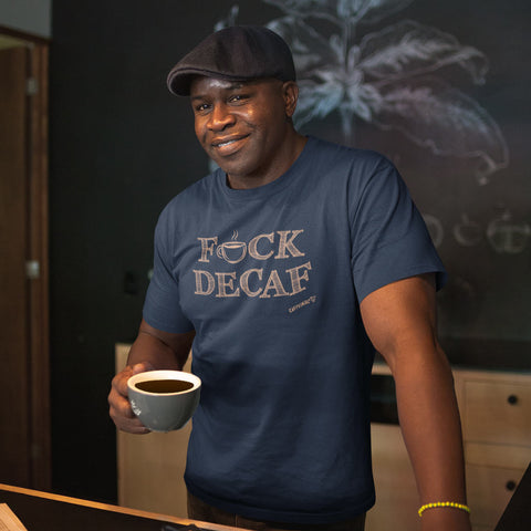 Image of A man holding a cup of coffee in a coffee shop wearing a hat and navy blue t-shirt with the caffeiniac design F_CK DECAF