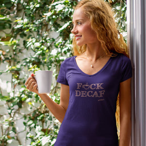 woman standing in a patio enjoying a cup of coffee, wearing a purple v-neck shirt with the Caffeiniac design F_CK DECAG in tan ink