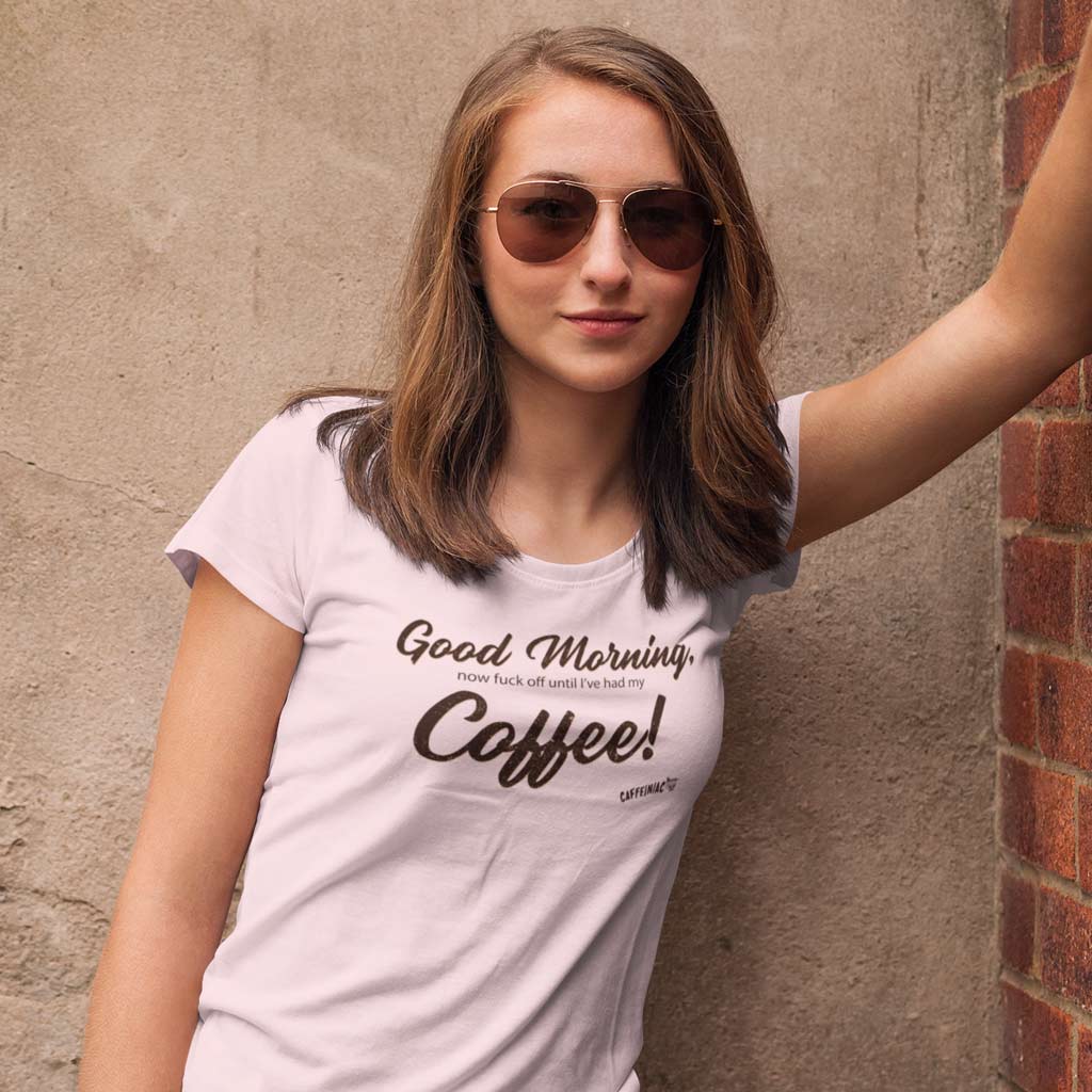 woman leaning against a brick wall wearing a pink Bella shirt featuring the Caffeiniac design Good Morning, now fuck off until I've had my Coffee!