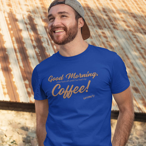 Image of A man standing near an aged building wearing a men's royal blue t-shirt featuring the Caffeiniac design "Good Morning, now fuck off until I've had my coffee!"  on the front of the tee in tan lettering