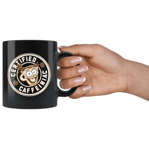 a hand holding a  black coffee mug featuring the Certified Caffeiniac design in tan and brown printed on the front and back